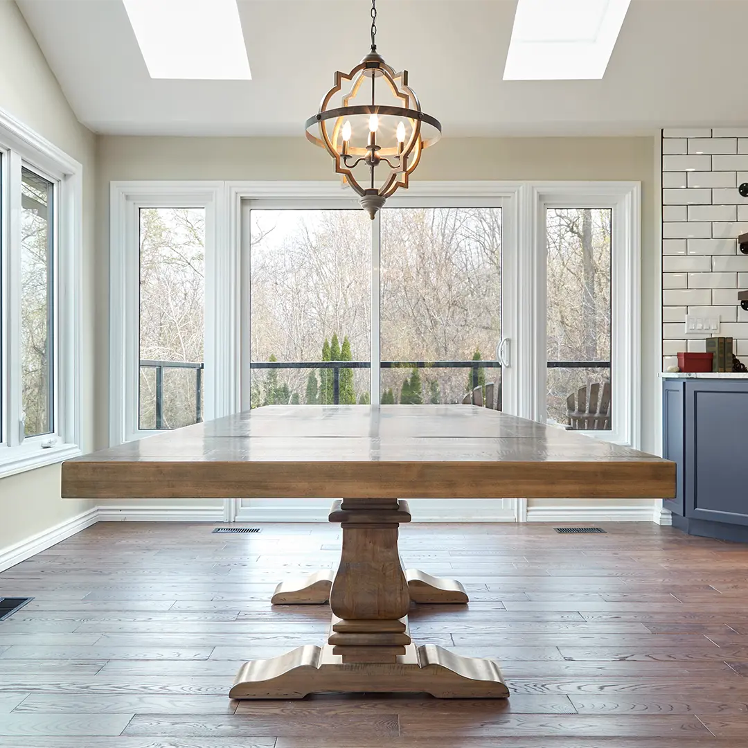 Black Sea solid wood pedestal dining table staged beside large windows